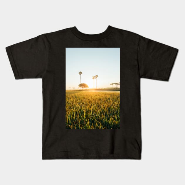 Sun Rising Over Grass Field in Burmese Countryside Kids T-Shirt by visualspectrum